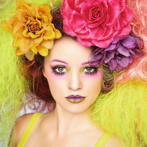 woman with mulit-colored red and yellow hair with large yellow, pink and purple flowers in her hair looking into the camera