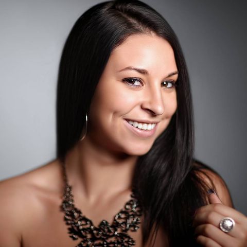 woman with long dark hair tilting her head to the side looking into the camera with one hand up showing her ring while holding her hair