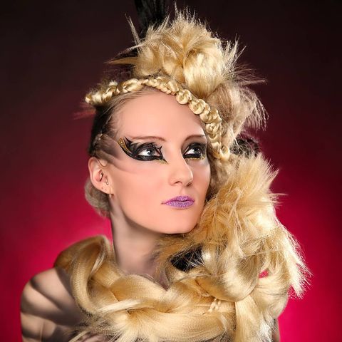 Woman with blonde and dark hair braided in large knots and laid around the front of her torso while she looks up and to her left in front of a red gradient background