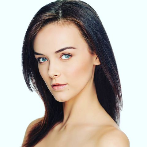 woman with long dark hair tilting her head to the side and downward looking into the camera from the bare shoulders up in front of a white background