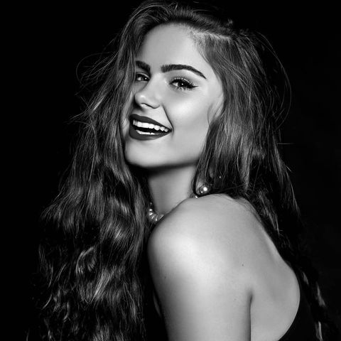 Black and white photo of a woman with dark wavy hair laughing in front of a black background