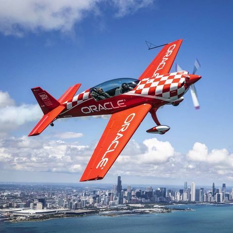 red plane turning sideways in mid air in front of a cityscape